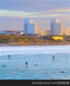 Aerial view of paddle surfing and surfers by Atlantic coast, scenic seascape with Baleal town in sunset light, Portugal
