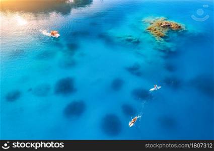 Aerial view of people on floating sup boards on blue sea, boat, rock, stones at sunset in summer in Oludeniz, Turkey. Tropical landscape. Kayaks on clear water. Active travel. Top view of canoe. Sport