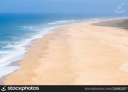 Aerial view of people sunbathing and playing on the wide empty endless sandy ocean beach at hot summer day