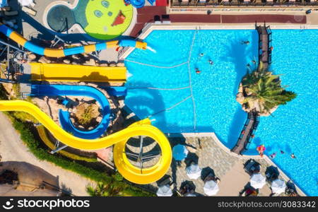 Aerial view of pool, aqua park, swimming people in transparent blue water, umbrellas, sunbeds, green trees at sunset. Summer holidays. Top view of water park. Water slides. Leisure in luxury resort