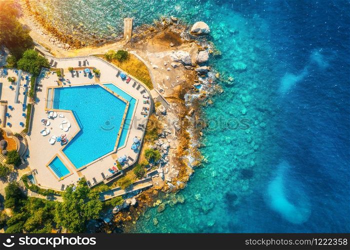 Aerial view of pool, sandy beach, stones, green trees, people and sea with transparent blue water at sunset. Top view of adriatic sea coast in summer. Landscape with azure water, rocks. Luxury resort