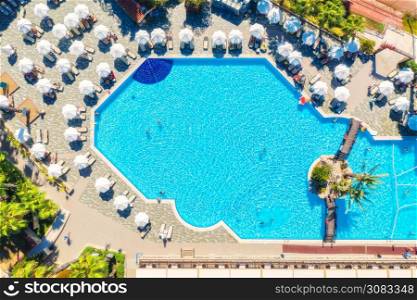 Aerial view of pool, swimming people in transparent blue water, umbrellas, sunbeds, green trees at sunset. Summer holidays. Top view of pool, deck chairs. Relax and leisure in luxury resort in Europe