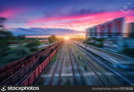 Aerial view of railroad and colorful sky with clouds at sunset with motion blur effect in summer. Industrial landscape with freight train, railway station, blurred background. Railway platform