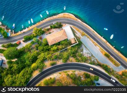 Aerial view of road, boats and yachts in water, buildings at sunset in spring. Colorful landscape with cars on roadway, sea coast, port, green trees in summer. Top view of highway in Croatia. Travel