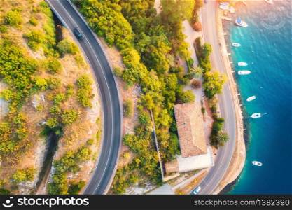 Aerial view of road, boats and yachts in water, buildings at sunset in summer. Colorful landscape with roadway, sea coast, port, green trees in spring. View from above of highway in Croatia. Travel. Aerial view of road, boats and yachts, buildings at sunset