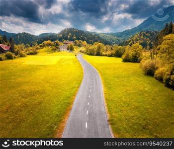 Aerial view of road in alpine meadows at sunset in autumn. Top view of rural road, mountains, forest in fall. Colorful landscape with country roadway, orange trees, hills, yellow grass in Slovenia