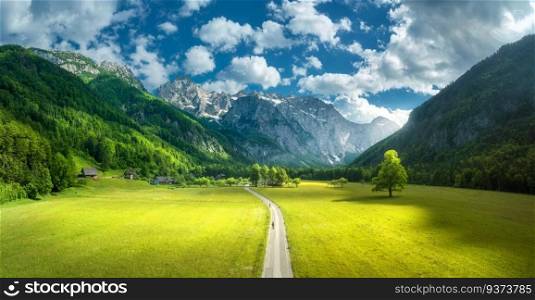 Aerial view of road in alpine mountains, green meadows, trees in summer. Top view of country road. Colorful landscape with road, rocks, field, grass, blue sky, sunbeam, clouds. Logar valley, Slovenia
