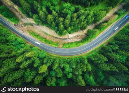 Aerial view of road in beautiful green forest at sunset in summer. Colorful landscape with roadway, pine trees, blurred cars and river in Carpatian mountains. Top view of highway. Travel in Ukraine