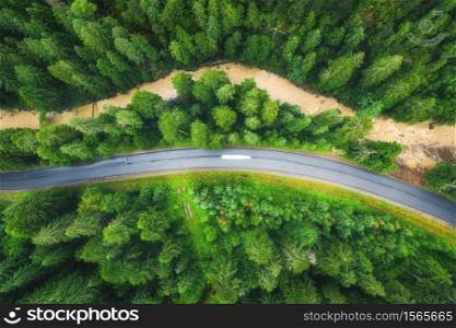 Aerial view of road in beautiful green forest at sunset in summer. Colorful landscape with roadway, pine trees, blurred car and river in Carpatian mountains. Top view of highway. Travel in Ukraine
