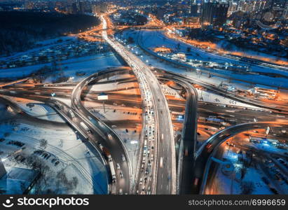 Aerial view of road in the modern city at night in winter. Top view of traffic in highway, buildings, illumination. Elevated road and Interchange overpass. Busy intersection. Expressway and motorway