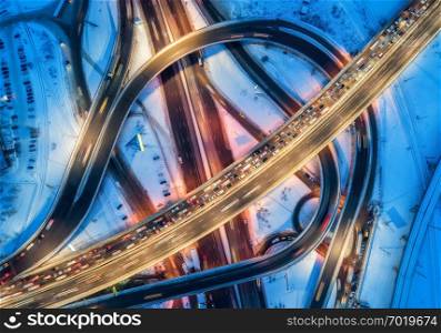 Aerial view of road in the modern city at night in winter. Top view of traffic in highway with city illumination. Cars on elevated road and interchange overpass. Busy intersection. Expressway at dusk