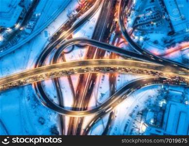 Aerial view of road in the modern city at night in winter. Top view of traffic in highway with city illumination. Cars on elevated road and interchange overpass. Busy intersection. Expressway at dusk