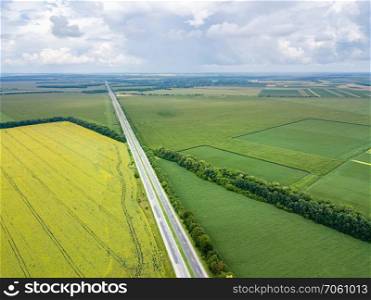 Aerial view of road through beautiful green field in the evening in summer. Beautiful landscape with speedway trees, green agricultural fields. Top view from flying drone.. Panoramic aerial view from drone of a highway with cars on it, fields, tree planting at summer sunset.