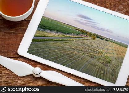aerial view of rural Nebraska landscape with a narrow road, meadow and corn field, reviewing image on a digital tablet