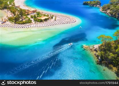 Aerial view of sandy beach, blue sea, speed boat at sunny day in summer. Motorboat in Blue Lagoon, sun beds, clear azure water. Tropical landscape with yacht, green trees. Top view. Oludeniz, Turkey