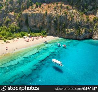 Aerial view of sandy beach, blue sea, yacht and boat, rock, umbrellas at summer sunny day. Butterfly Valley in Oludeniz, Turkey. Top drone view of sea coast, swimming people, clear azure water. Travel