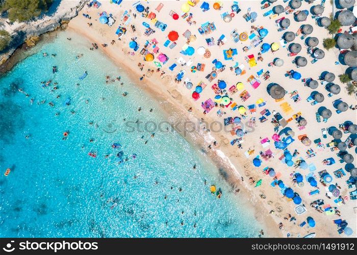 Aerial view of sandy beach with colorful umbrellas, swimming people in sea bay with transparent blue water at sunset in summer. Travel in Mallorca, Balearic islands, Spain. View from above. Landscape