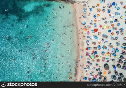 Aerial view of sandy beach with colorful umbrellas, swimming people in sea bay with crystal clear blue water in sunny morning in summer. Travel in Balearic islands. Top view from drone. Landscape
