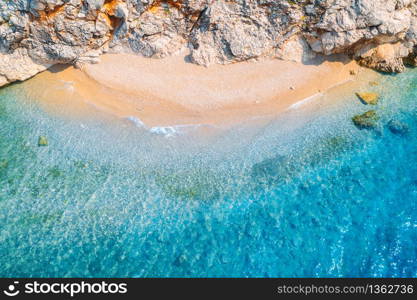 Aerial view of sandy beach with rocks and sea with transparent blue water at sunset. Coast of adriatic sea at sunset in summer. Top view. Landscape with clear azure water, waves, stones. Nature