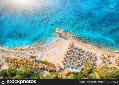 Aerial view of sandy beach with umbrellas, green forest at sunrise in summer. Blue lagoon in Oludeniz, Turkey. Tropical landscape with sea bay, island, white sandy bank, blue water. Top view. Nature