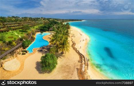 Aerial view of sea coast. Sandy beach with pool, palms and umbrellas at sunset. Summer holiday on Indian Ocean, Zanzibar, Africa. Tropical landscape with palm trees, hotels, sand, blue water. Top view