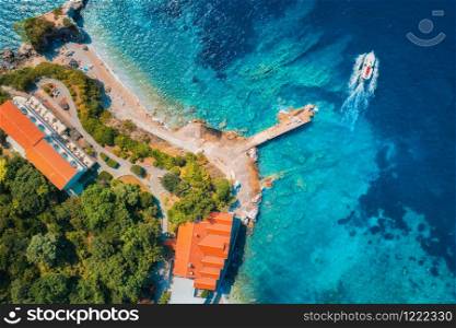 Aerial view of sea coast with clear blue water, boats, pier, hotels and green trees in summer at sunny day in Croatia. Top view of sandy beach, floating yacht, buildings and forest. Travel