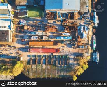 Aerial view of ships and boats in dry dock for repairs. Top view of iron rusting ship is in dry dock for refurbishing. Industrial scene with old yachts, buildings, tree and football field at sunset. Aerial view of ships and boats in dry dock. Aerial view of ships and boats in dry dock