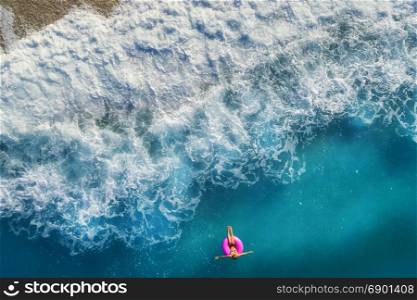 Aerial view of slim woman swimming on the pink swim ring in the transparent turquoise sea in Oludeniz,Turkey. Summer seascape with girl, beautiful waves, blue water in sunny day. Top view from drone