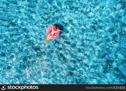 Aerial view of slim young woman swimming on the pink donut swim ring in blue sea at sunny day. Tropical aerial landscape with girl, clear water in Europe. Top view. Summer travel. Holiday