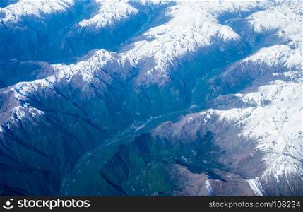 Aerial view of snow-capped mountains and green valleys in the European alps during summer.