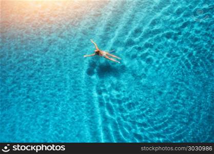 Aerial view of swimming woman at sunset in Maldives. Mediterranean sea. Aerial seascape with young girl, clear blue water, waves in summer. Transparent water. Top view. Resort on seashore. Holiday . Aerial view of swimming woman in mediterranean sea at sunset