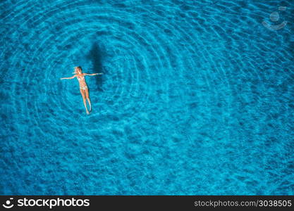 Aerial view of swimming woman at sunset in Maldives. Mediterranean sea. Aerial seascape with young girl, clear blue water, waves in summer. Transparent water. Top view. Resort on seashore. Holiday. Aerial view of swimming woman in mediterranean sea. Aerial view of swimming woman in mediterranean sea at sunset