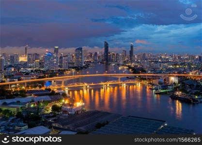 Aerial view of Taksin Bridge with Chao Phraya River, Bangkok Downtown. Thailand. Financial district and business centers in smart urban city. Skyscraper and high-rise buildings at night.
