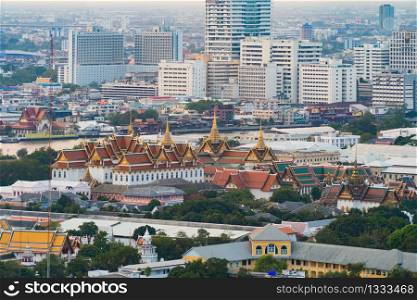 Aerial view of Temple of the Emerald Buddha, Wat Phra Kaew, and skyscraper buildings. Bangkok downtown area at sunset time, Thailand. Buddhist temple. Thai architecture.