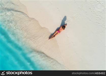 Aerial view of the beautiful young lying woman on the white sandy beach near sea with waves at sunset. Summer holiday. Top view of the back of sporty slim girl, clear azure water. Sexy buttocks. Relax