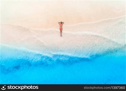 Aerial view of the beautiful young woman lying on the white sandy beach near sea with waves at sunset. Summer travel. Top view of slim girl, transparent blue water. Indian Ocean in Zanzibar, Africa. Aerial view of the young woman lying on the white sandy beach