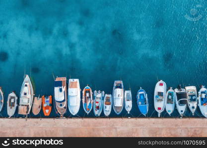 Aerial view of the boats and yachts on tropical sea coast at sunset in summer. Colorful landscape with pier, boat, ocean with transparent blue water. Top view of motorboats in harbor. Travel