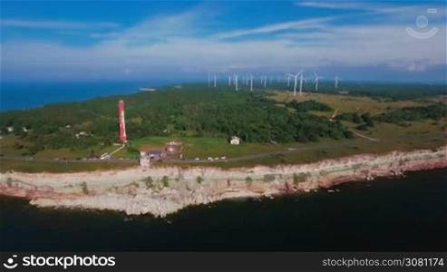 Aerial view of the coastline with rocks from the sea and on the land old lighthouse and wind turbine