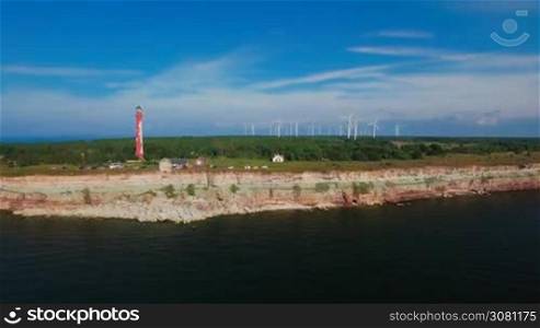 Aerial view of the coastline with rocks from the sea and on the land old lighthouse and wind turbines