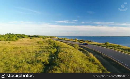 Aerial view of the driving black car on the road along the cliff next the sea in summer at sunset