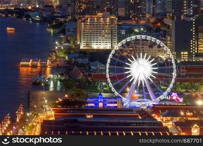 Aerial view of the ferris wheel, Asiatique The Riverfront, near Chao Phraya River with skyscraper buildings in Bangkok Downtown at night, urban city, Thailand.