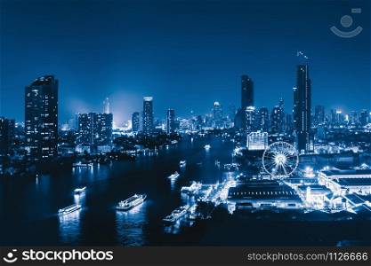 Aerial view of the ferris wheel with boats, Asiatique The Riverfront, near Chao Phraya River with skyscraper buildings in Bangkok Downtown at night, urban city, Thailand.