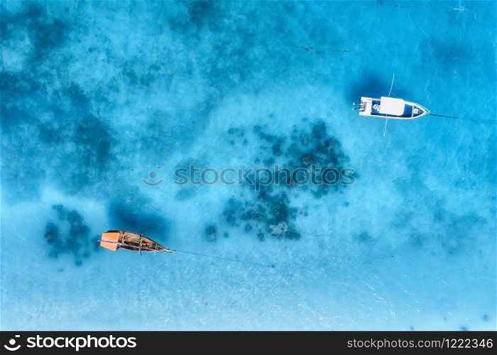 Aerial view of the fishing boat and yacht in clear blue sea at sunset in summer. Top view from drone of yachts, sandy beach. Travel in Zanzibar, Africa. Tropical landscape with motorboat, water