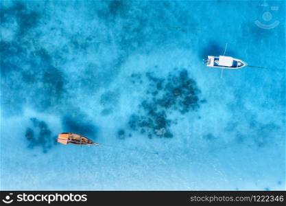 Aerial view of the fishing boat and yacht in clear blue sea at sunset in summer. Top view from drone of yachts, sandy beach. Travel in Zanzibar, Africa. Tropical landscape with motorboat, water