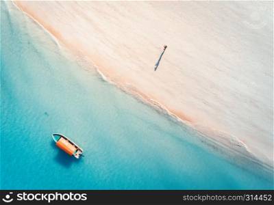 Aerial view of the fishing boat in clear blue water and man on the sandy beach at sunset in summer. Top view of boat. Indian ocean. Travel in Zanzibar, Africa. Landscape with motorboat, sea. Seascape