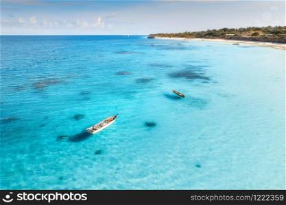 Aerial view of the fishing boat in clear blue water at sunny day in summer. Top view of boat, sandy beach, palm trees. Indian ocean. Travel in Zanzibar, Africa. Colorful landscape with yacht, sea