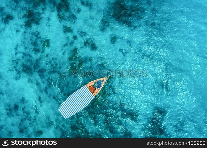 Aerial view of the fishing boat in clear blue water at sunny day in summer. Top view from drone of boat in Indian ocean in Zanzibar, Africa. Landscape with motordboat, transparent sea. Seascape
