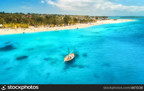 Aerial view of the fishing boat in clear blue water at sunny day in summer. Top view of boat, sandy beach, palm trees. Indian ocean. Travel in Zanzibar, Africa. Colorful landscape with sailboat, sea