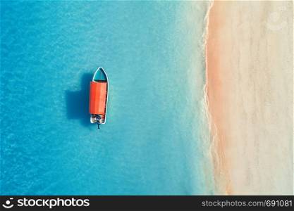 Aerial view of the fishing boat in clear blue water at sunny day in summer. Top view from the air of boat, sandy beach. Indian ocean in Zanzibar, Africa. Landscape with motorboat and clear sea. Travel