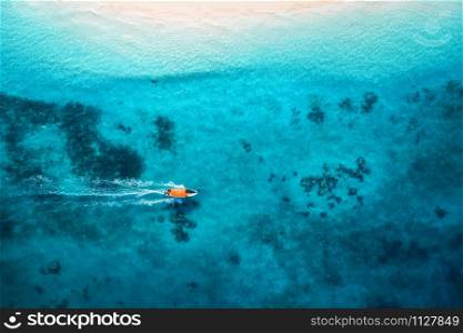 Aerial view of the fishing boat in clear blue water at sunset in summer. Top view from the air of boat, sandy beach. Indian ocean in Zanzibar, Africa. Landscape with motorboat and clear sea. Travel